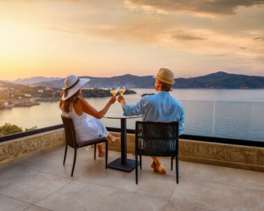 A elegant holiday couple enjoys the beautiful summer sunset in the mediterranean sea with a glass of wine, romantic honeymoon vacation concept