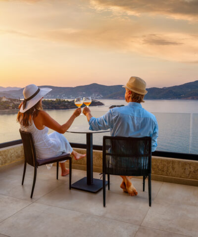 A elegant holiday couple enjoys the beautiful summer sunset in the mediterranean sea with a glass of wine, romantic honeymoon vacation concept