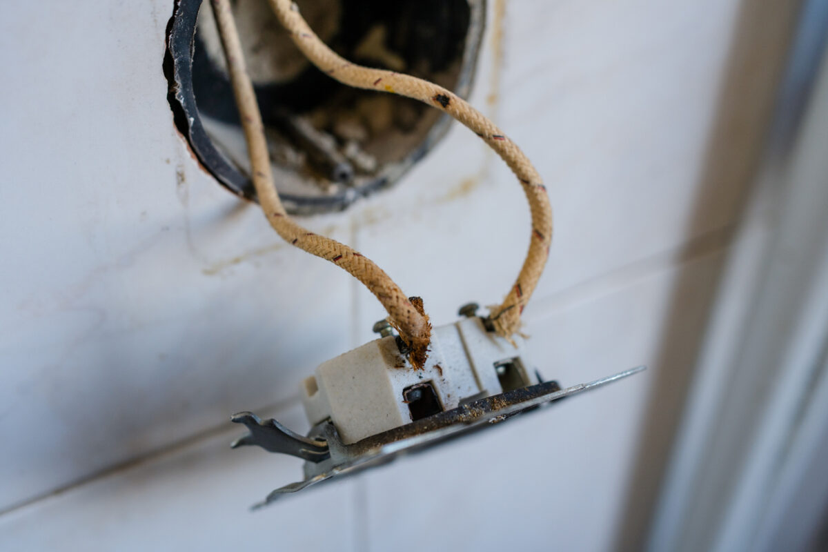 Close-up of old-fashioned cloth insulated electrical wiring in a wall socket. Perfect for showing fire hazards, outdated electrical standards, and home renovation in vintage buildings.