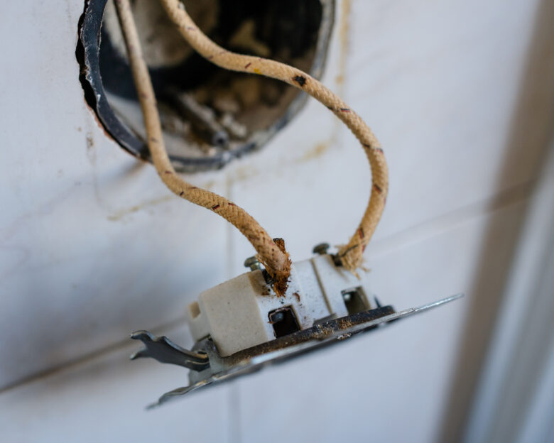 Close-up of old-fashioned cloth insulated electrical wiring in a wall socket. Perfect for showing fire hazards, outdated electrical standards, and home renovation in vintage buildings.