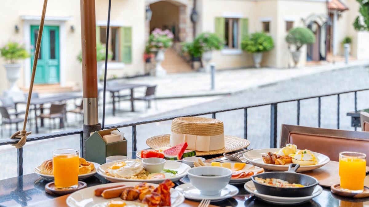 Breakfast table served with eggs, juice and fruit on an outdoor terrace overlooking a cobblestone street. Luxury travel lifestyle and morning dining in a European style village.