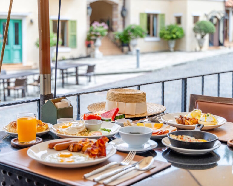 Breakfast table served with eggs, juice and fruit on an outdoor terrace overlooking a cobblestone street. Luxury travel lifestyle and morning dining in a European style village.