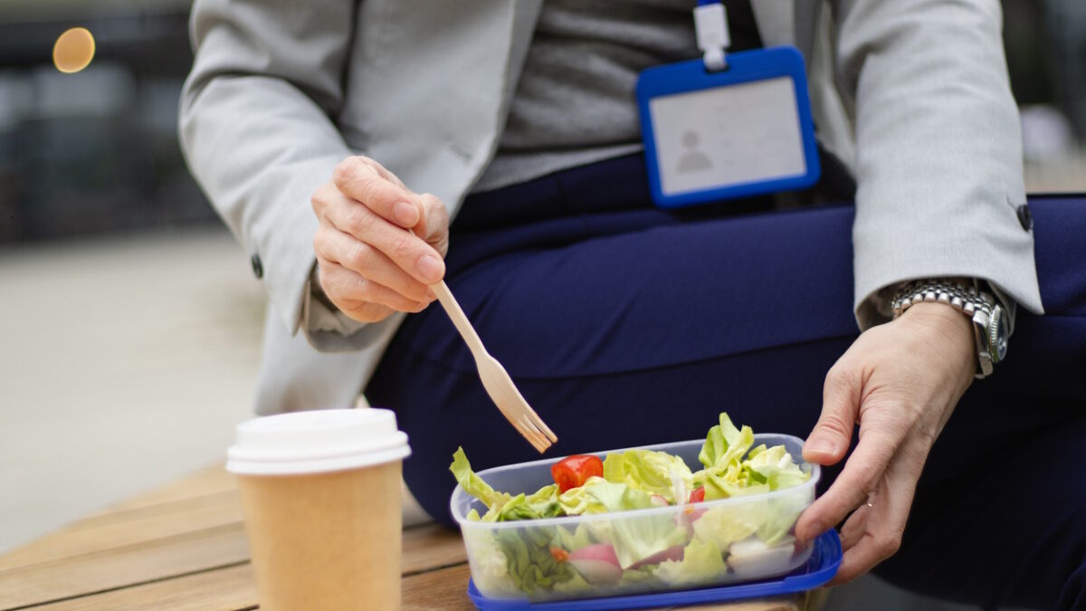 unrecognizable business person with accreditation card eating salad and sitting on a bench during a break of a business meeting