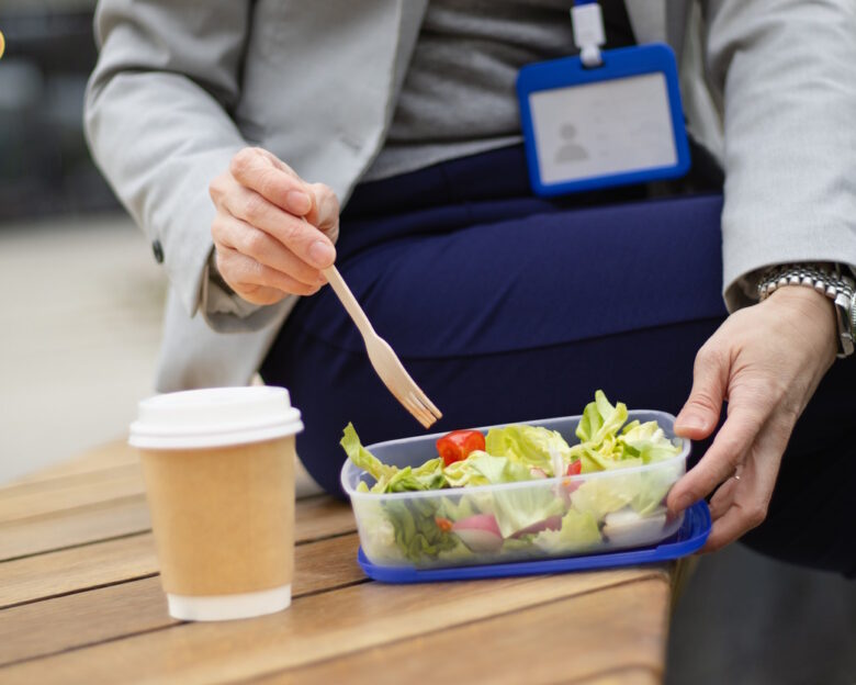unrecognizable business person with accreditation card eating salad and sitting on a bench during a break of a business meeting