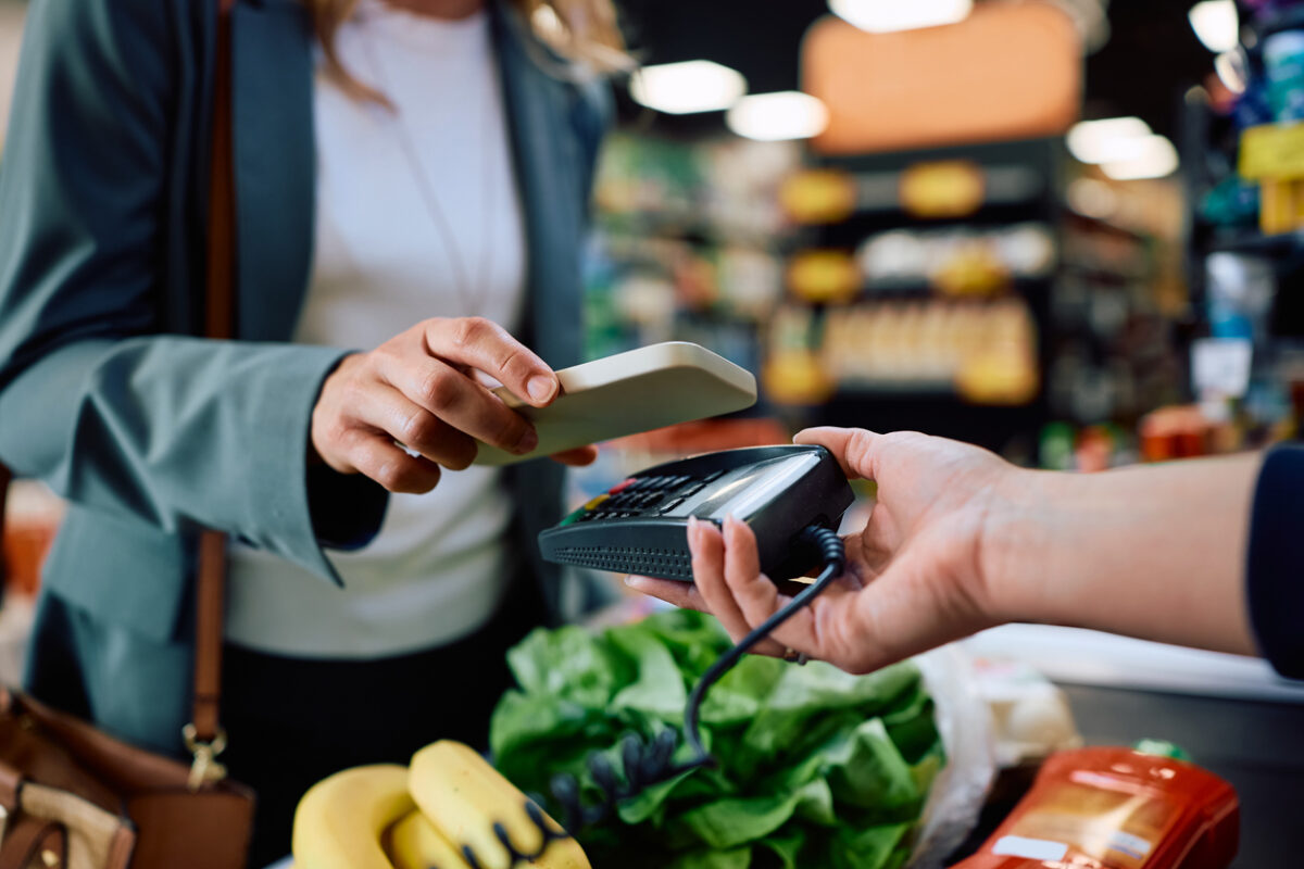 Close up of supermarket customer using cell phone app while paying at cash register.