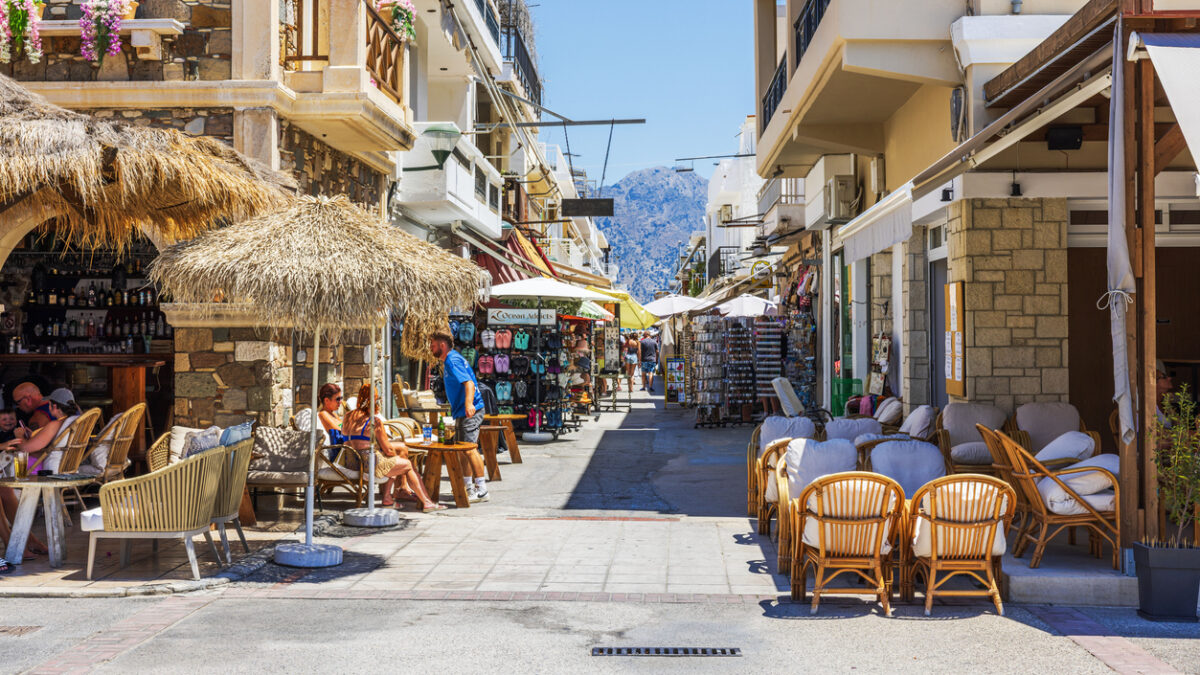 Greece. Kardamena. July 07.2025. Beautiful view of cozy Mediterranean street with outdoor cafes shops and mountains in sunny resort town.