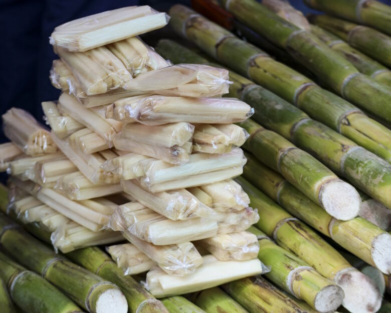 Bundles of raw sugar cane sit beside plastic-wrapped peeled sticks at a local produce stall.