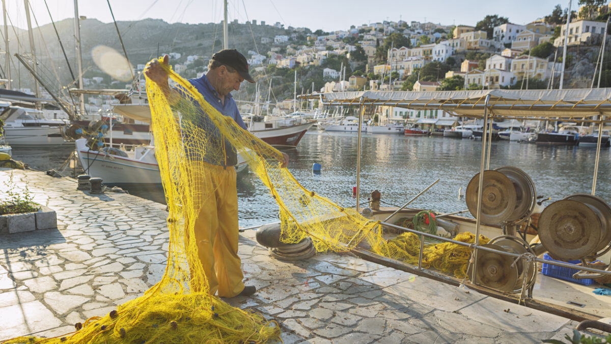 Symi, Greece - Greek fisherman working in Symi Harbour. Symi is a Greek island and municipality. The island has 2,580 inhabitants, mostly engaged in tourism, fishing, and trade.