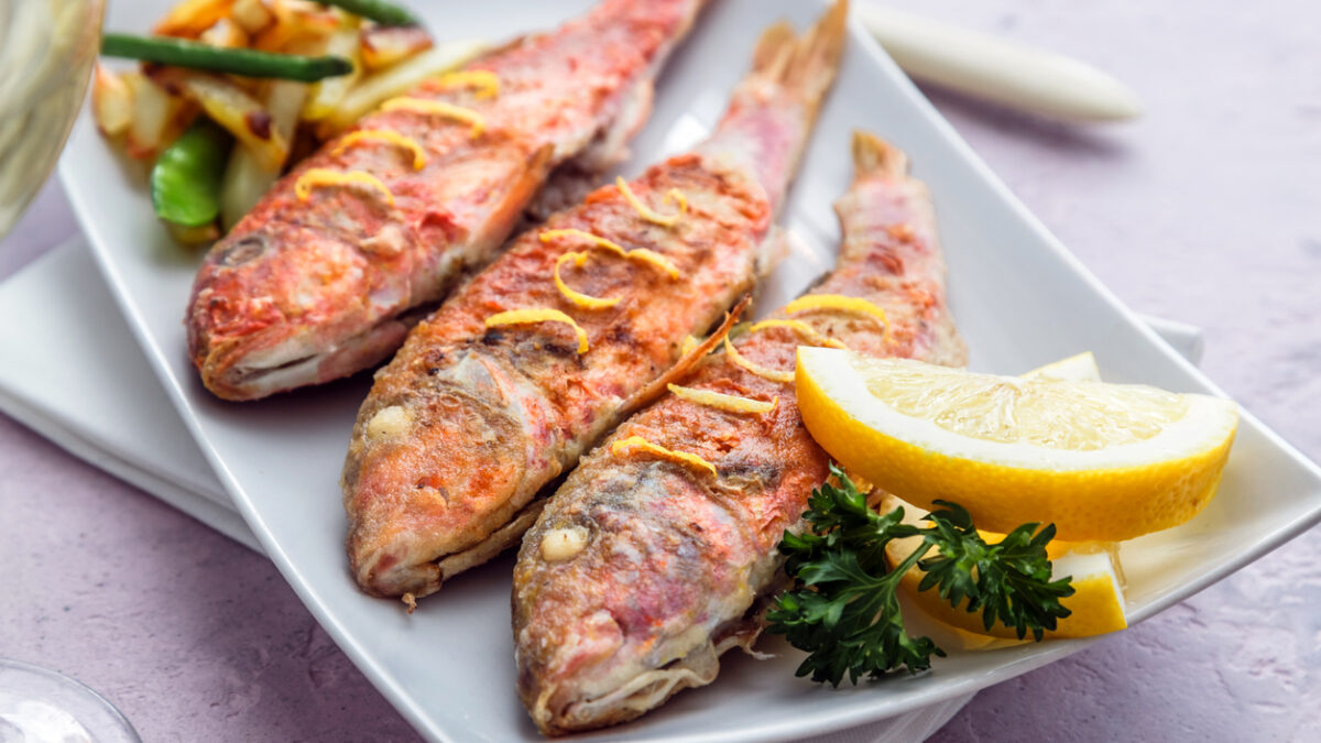Plate of fried small fish red mullet and lemon, close view.