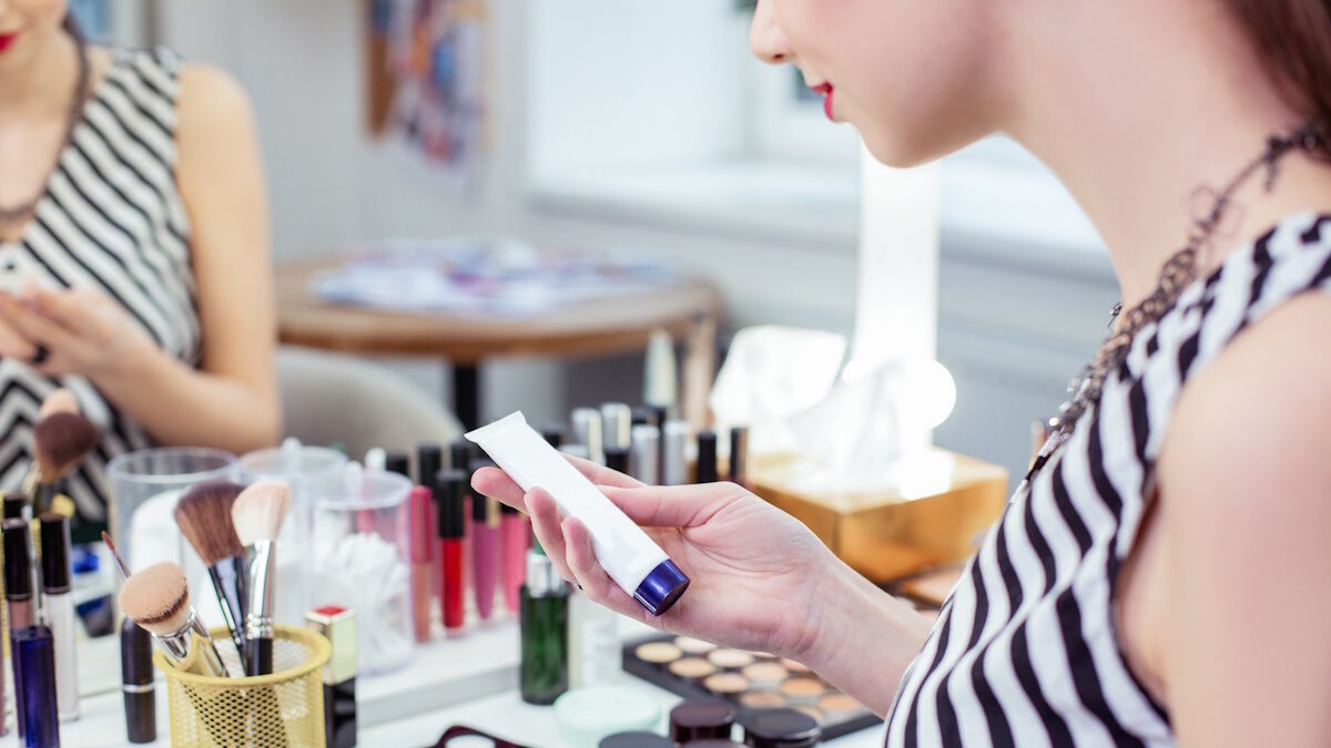 Facial cream. Pleasant young woman sitting in front of the mirror while using her facial cosmetics