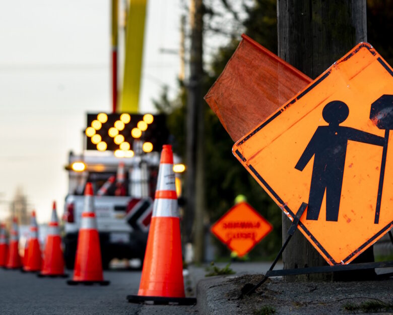 Lane closure on a busy road due to maintenance signs detour traffic temporary street work orange lighted arrow, barrels, and cones.