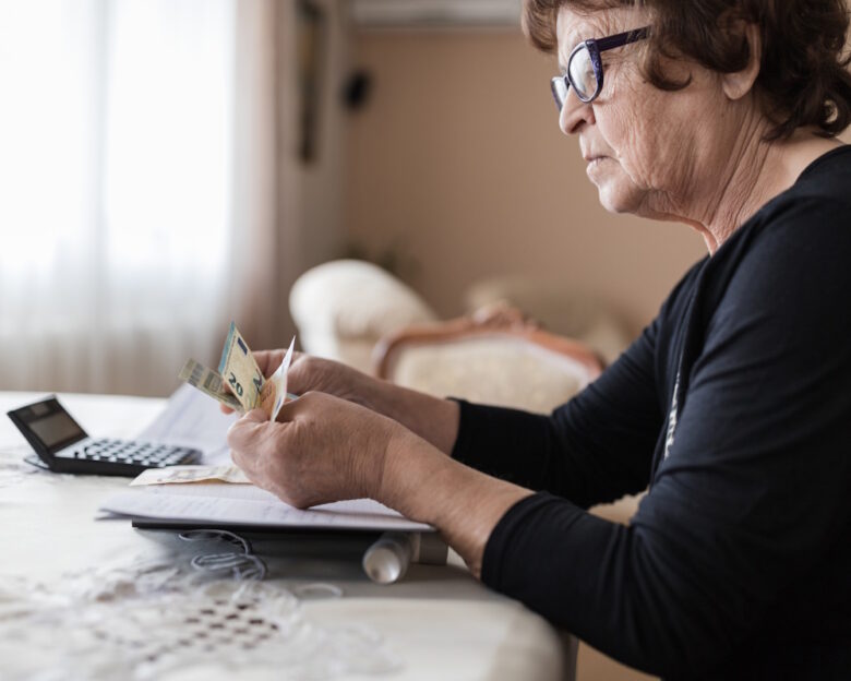 Worried older woman sitting at a table and calculating her expenses
