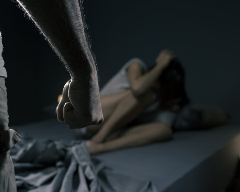 Man threatening a woman in the bedroom, she is scared and lying in bed, domestic violence concept