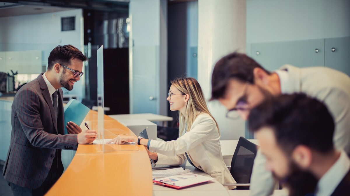 A young man is standing at a bank counter. Because of the good negotiation skills of an efficient employee, he decided to cooperate with her and sign a contract.