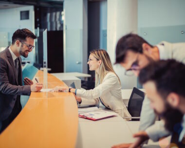 A young man is standing at a bank counter. Because of the good negotiation skills of an efficient employee, he decided to cooperate with her and sign a contract.
