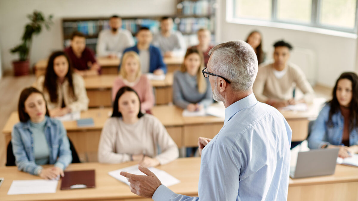 Rear view of mature teacher talking to his student during lecture at university classroom.