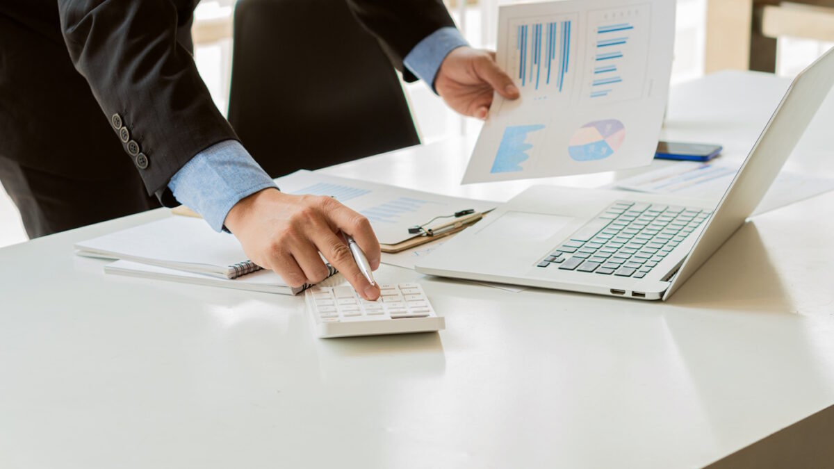 At the accounting desk, an accountant presses a calculator to analyze investment charts to generate monthly financial reports or company profits.