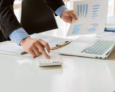 At the accounting desk, an accountant presses a calculator to analyze investment charts to generate monthly financial reports or company profits.