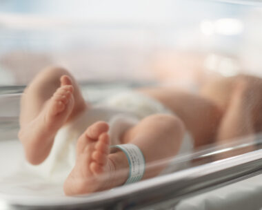 Cute Little Caucasian Newborn Baby Lying in Bassinet in a Maternity Hospital. Portrait of a Tiny Playful and Energetic Child with a Name ID Tag on the Leg. Healthcare, Pregnancy and Motherhood Concept