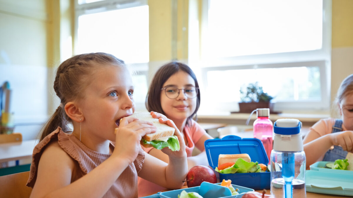 Group of school girls eating lunch, sitting at the table, lunch boxes on the table.
