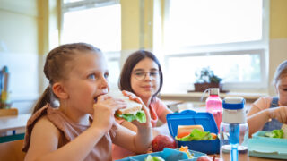 Group of school girls eating lunch, sitting at the table, lunch boxes on the table.