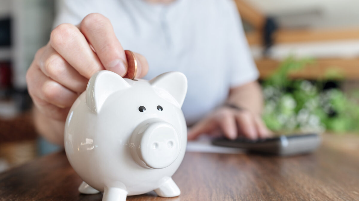 Man putting a coin into a pink piggy bank concept for savings and finance