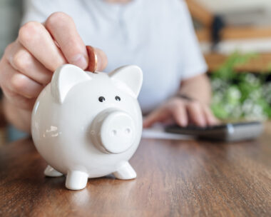 Man putting a coin into a pink piggy bank concept for savings and finance