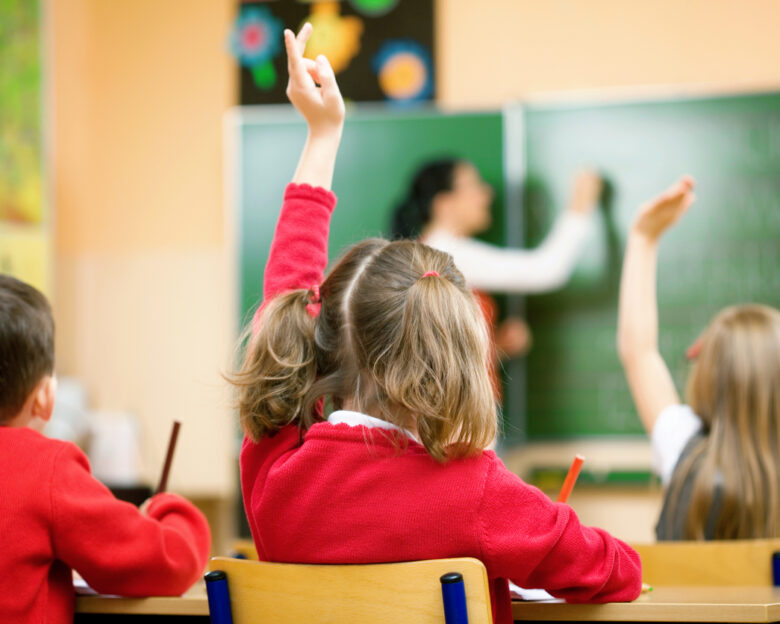Elementary school kids raising their hands in class to answer a teacher's question.