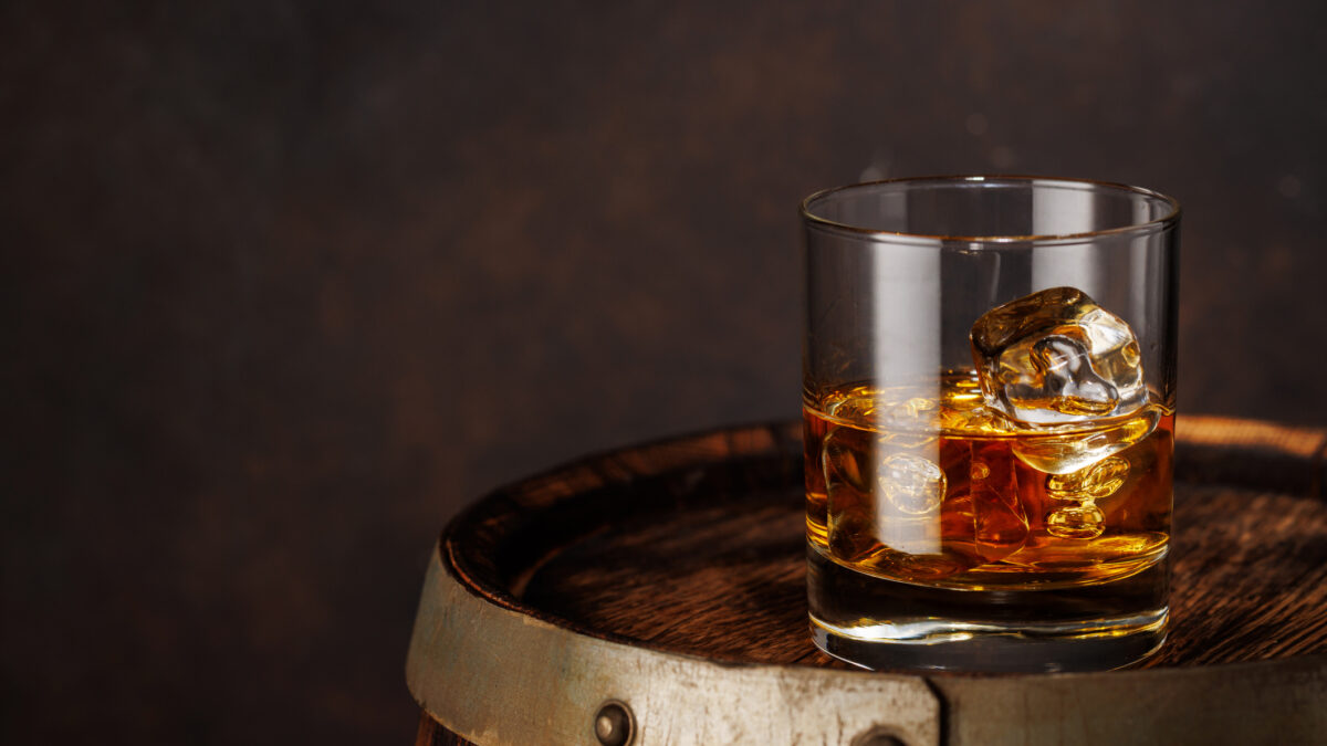 A classic whiskey glass filled with golden amber whiskey, placed on a wooden barrel