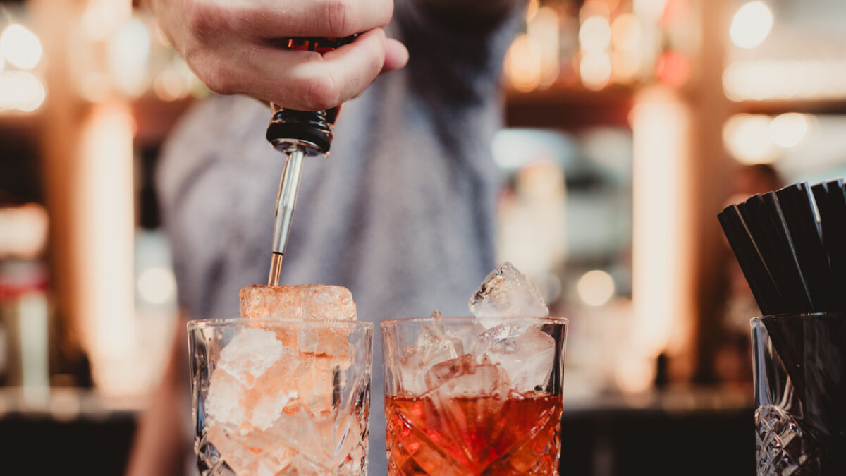 Bartender pouring alcohol into drinks into glasses with ice at bar