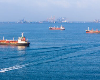 LPG gas and oil tanker ships anchored in the ocean, with a fast patrol boat in the foreground. Global energy transport, war energy crisis, and Strait of Hormuz blockade concept.