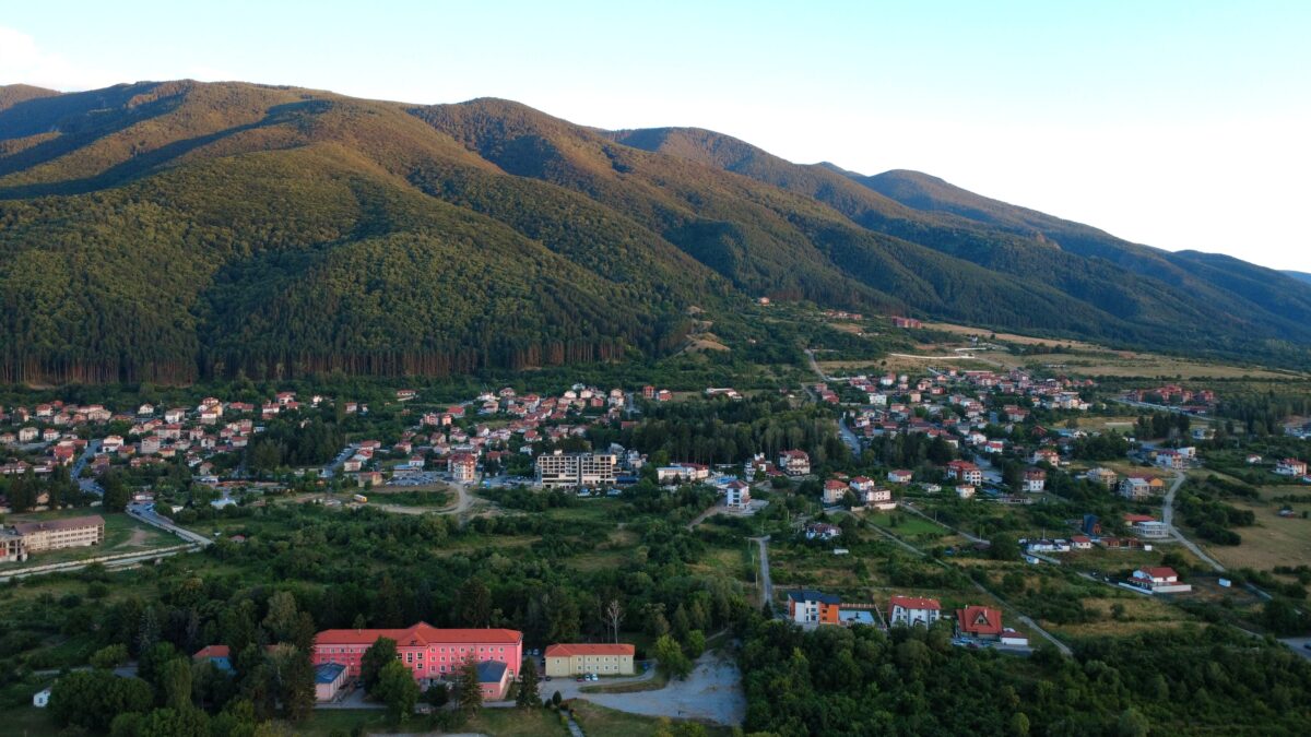 Aerial view of a small town nestled at the foot of forested mountains during golden hour light.