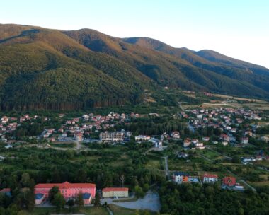 Aerial view of a small town nestled at the foot of forested mountains during golden hour light.