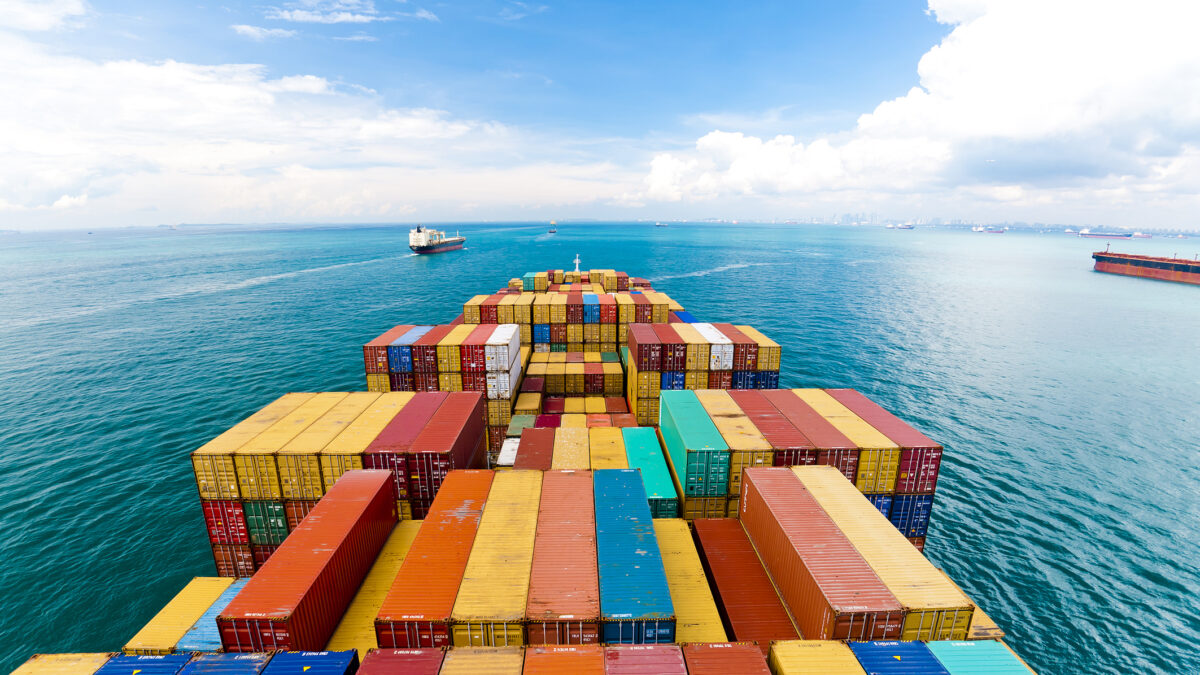 Horizontal wide angle view of heavy loaded container cargo ship in busy strait of Malacca.