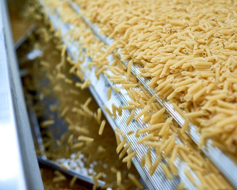 Close up of dry macaroni spilling from machine unit on modern food production factory, copy space