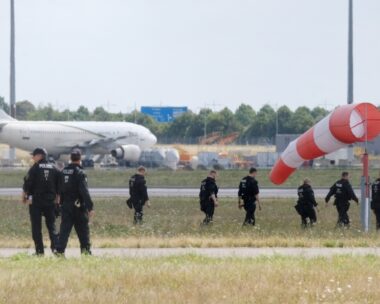 07 August 2026, Saxony, Schkeuditz: Police officers are walking across a field on the grounds of Leipzig Airport. The investigation into the discovery of the explosive-laden drone is ongoing. Numerous police officers are on the scene near the northern runway, searching the area on foot.