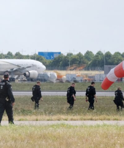 07 August 2026, Saxony, Schkeuditz: Police officers are walking across a field on the grounds of Leipzig Airport. The investigation into the discovery of the explosive-laden drone is ongoing. Numerous police officers are on the scene near the northern runway, searching the area on foot.