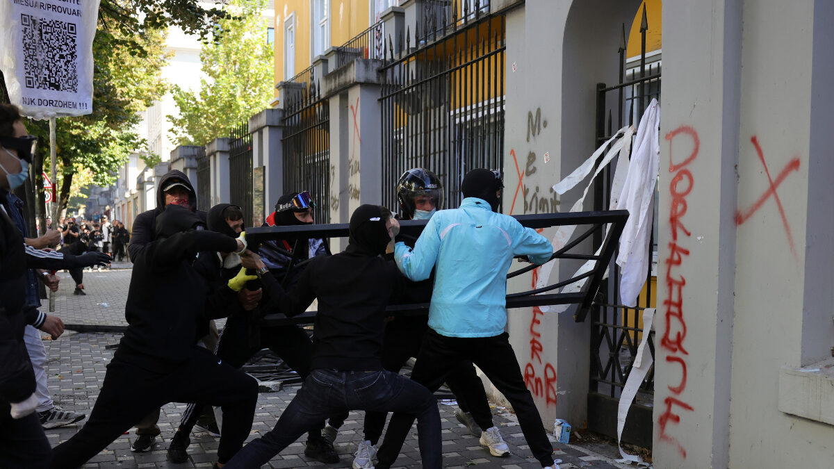 Hooded protesters try to break through a gate at the Education Ministry as the Albanian word "Resign" is displayed on a wall during clashes in Tirana, Albania, Tuesday, Oct. 13, 2026, joining a demonstration organized by the Flamingo protest movement demanding the resignation of Prime Minister Edi Rama.
