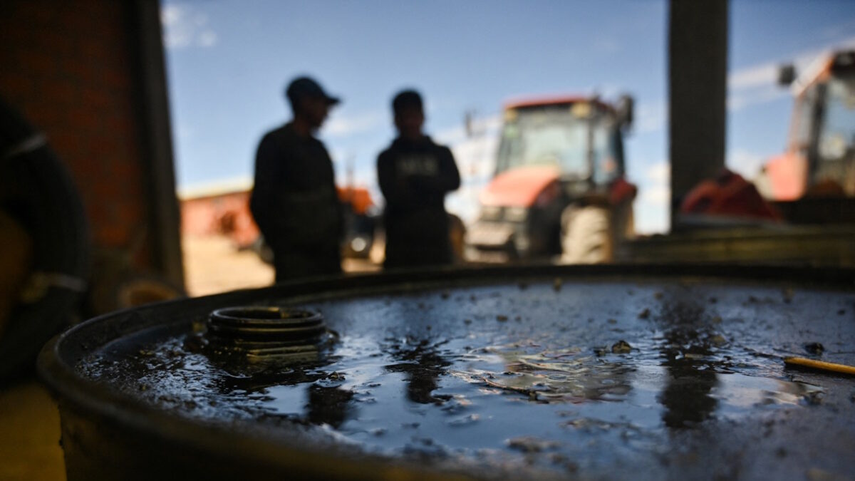 Etson Machaca and Vidal Machaca talk on the background, behind a container coated with oil obtained at the small-scale pyrolysis plant that converts waste, mainly plastic and rubber tires, into fuel used to power his agricultural equipment, in Ancocala, Bolivia, October 9, 2026