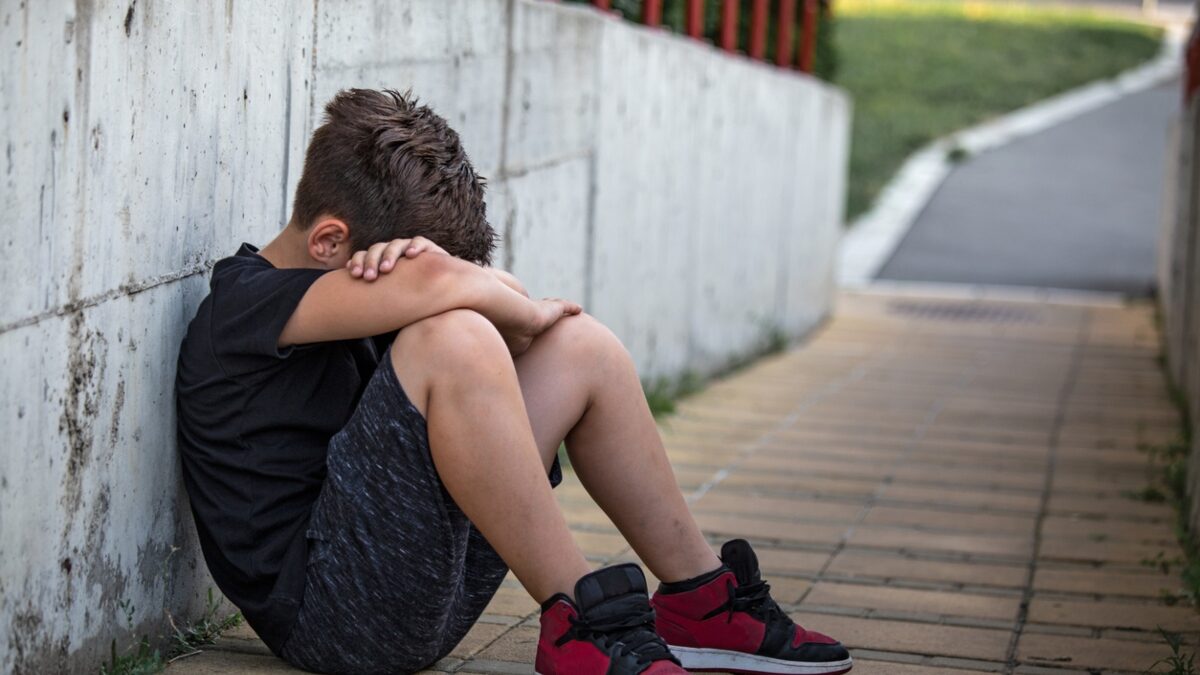 Little boy sad sitting alone at school hides his face. Isolation and bullying concept. Kid sad and unhappy, child was crying, upset, feel sick