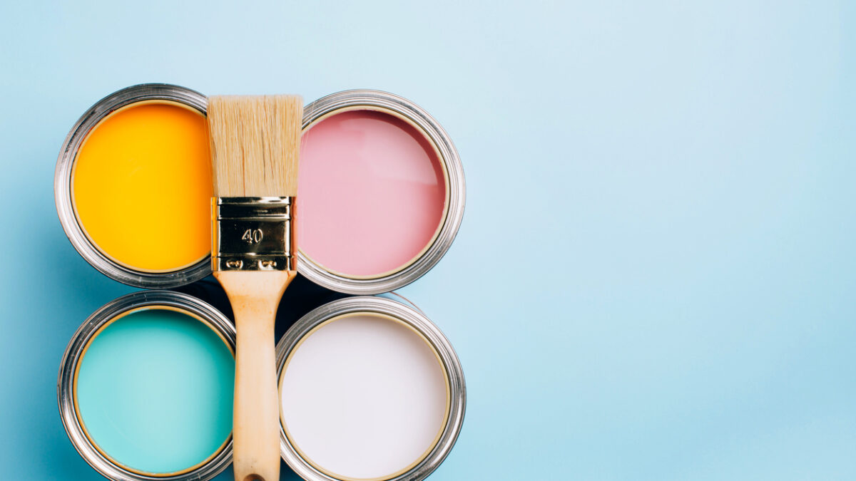 Brush with wooden handle on open cans on blue pastel background. Yellow, white, pink, turquoise colors. Renovation concept. Place for text.