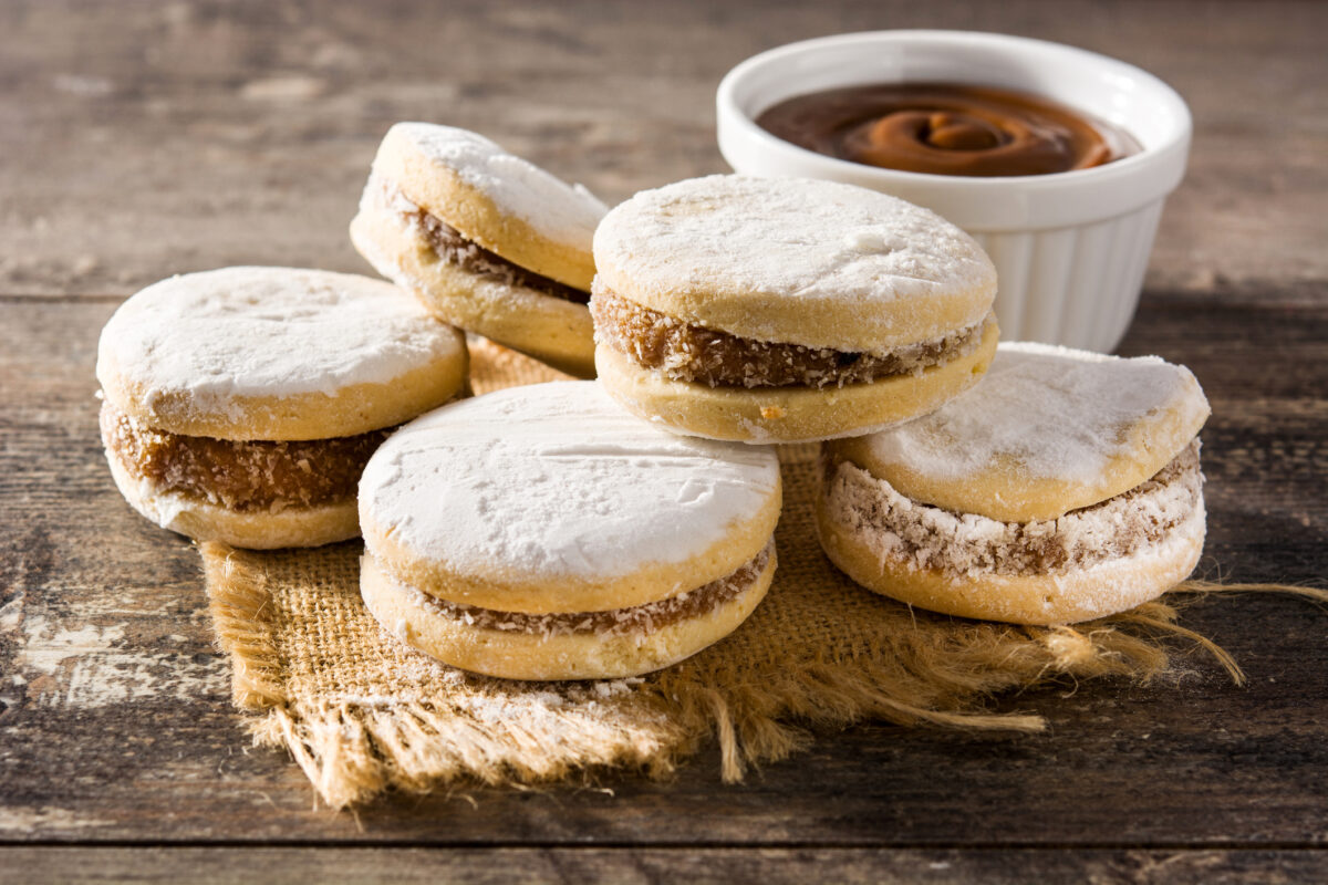 Traditional Argentinian alfajores with dulce de leche and sugar on wooden table.