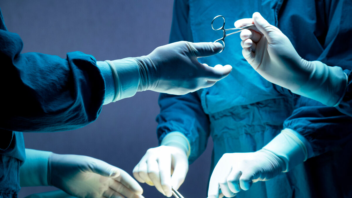 doctor and nurse medical team are performing surgical operation at emergency room in hospital. assistant hands out scissor and instruments to surgeons during operation.