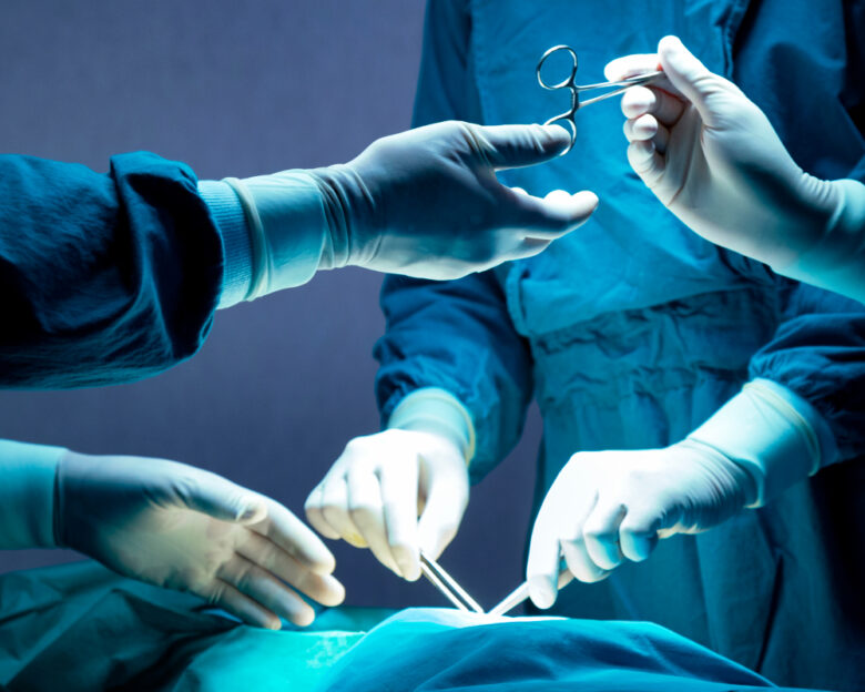 doctor and nurse medical team are performing surgical operation at emergency room in hospital. assistant hands out scissor and instruments to surgeons during operation.