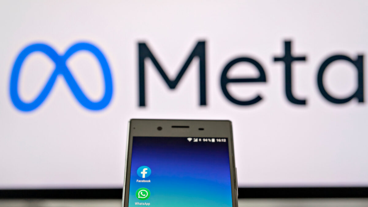 Smartphone display with logo of Facebook, WhatsApp and Instagram apps in hand against blurred META logotype on white monitor background: Tallinn, Estonia - October 29, 2021