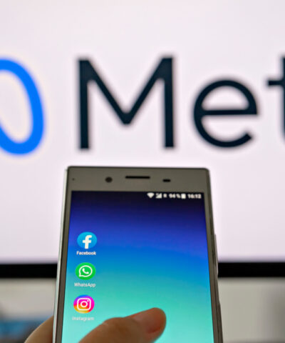 Smartphone display with logo of Facebook, WhatsApp and Instagram apps in hand against blurred META logotype on white monitor background: Tallinn, Estonia - October 29, 2021
