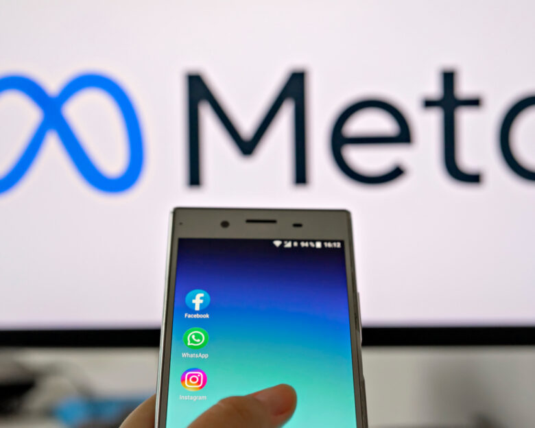 Smartphone display with logo of Facebook, WhatsApp and Instagram apps in hand against blurred META logotype on white monitor background: Tallinn, Estonia - October 29, 2021