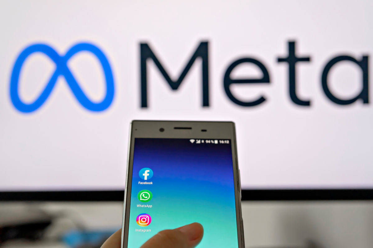 Smartphone display with logo of Facebook, WhatsApp and Instagram apps in hand against blurred META logotype on white monitor background: Tallinn, Estonia - October 29, 2021