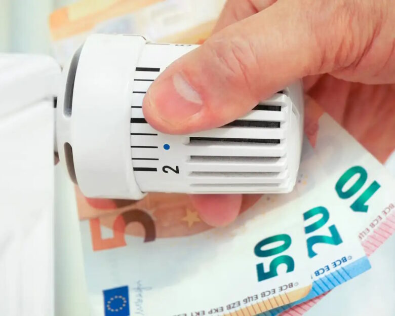 Hand on the heating thermostat with money bills, heating costs concept