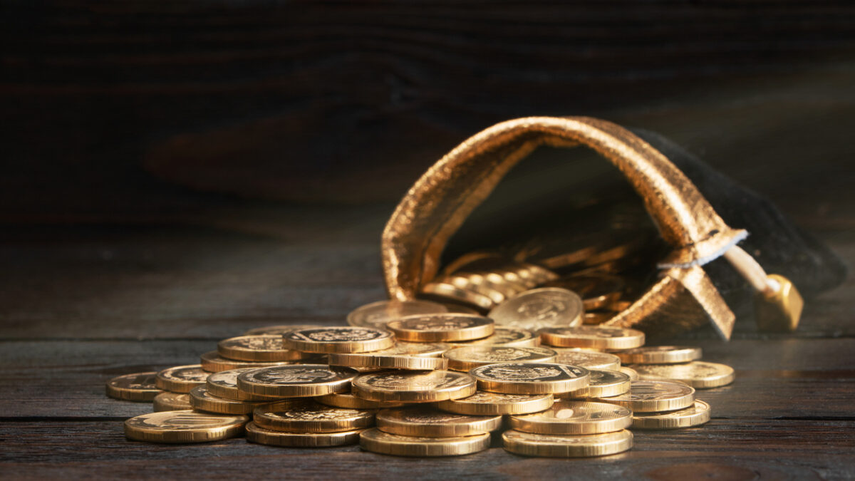 A bag with gold coins on a wooden background. The money in a black bag on a wooden table. Treasure Hunt. A Purse with money. Wallet wit gold coins
